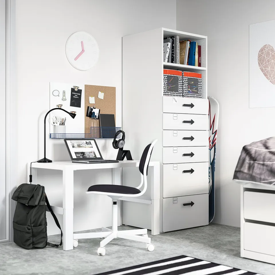 Modern white study desk with black chair, laptop, headphones, and grey backpack under minimalist decor.