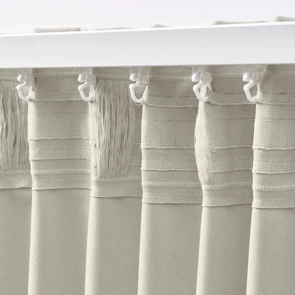 Beige KORGMOTT curtains hang from hooks, showing their textured fabric and block-out design, ideal for privacy and light control.