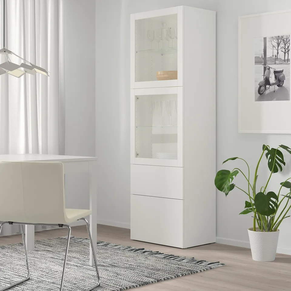 White BESTÅ cabinet, tall, glass doors, wooden floor, modern living room setup.