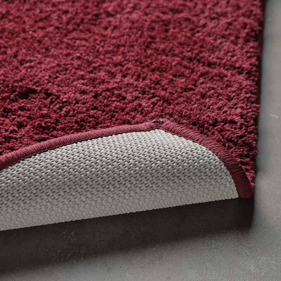 Close-up of burgundy bath mat with white latex backing, showing soft texture and non-slip detail.