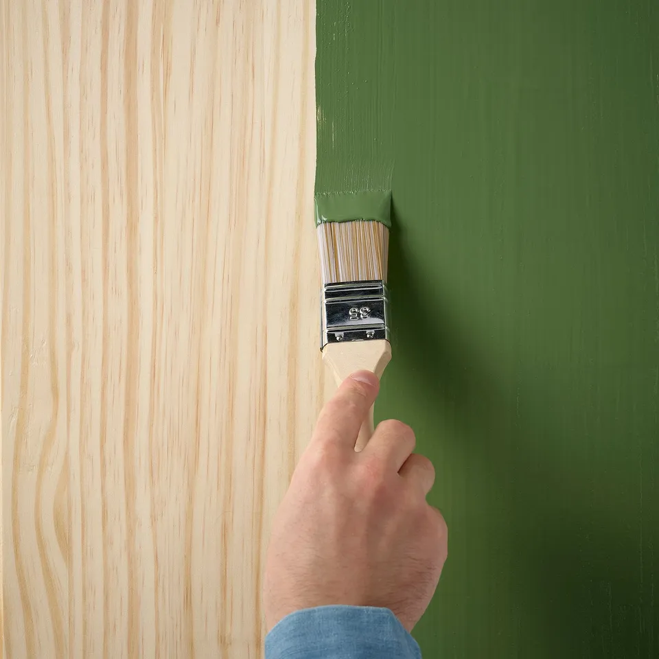 Hand painting wooden furniture with green paint using a brush.
