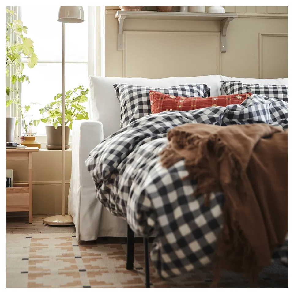 Cosy bedroom with black & white checked bedding, tall plant, earthy rug.