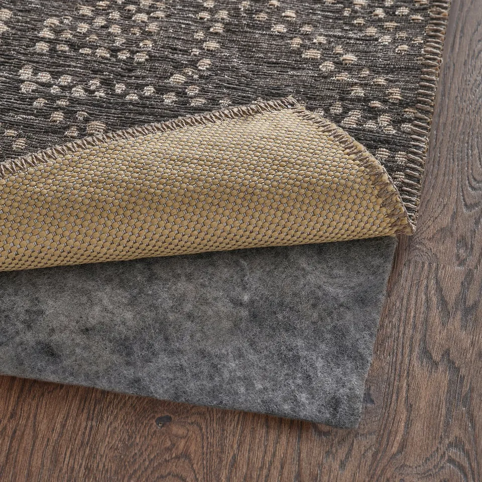 Grey woven rug with a fold-over edge on a wooden floor. The rug has visible backing, likely for added durability or non-slip purposes.