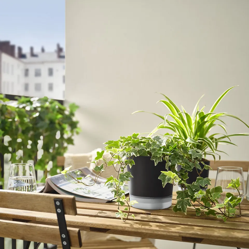 Outdoor wooden table with black VÅRDTRÄD self-watering pots and plants.