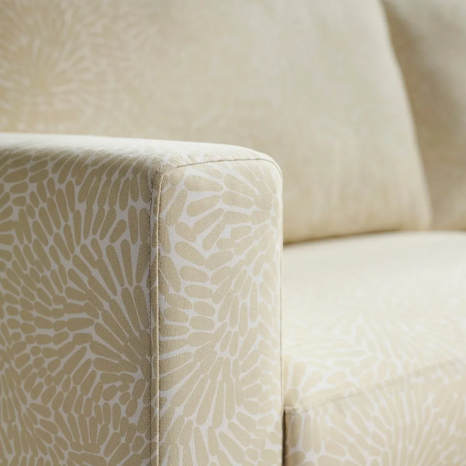Close-up of stylish sofa corner, showcasing intricate, floral-patterned fabric and precise upholstery.