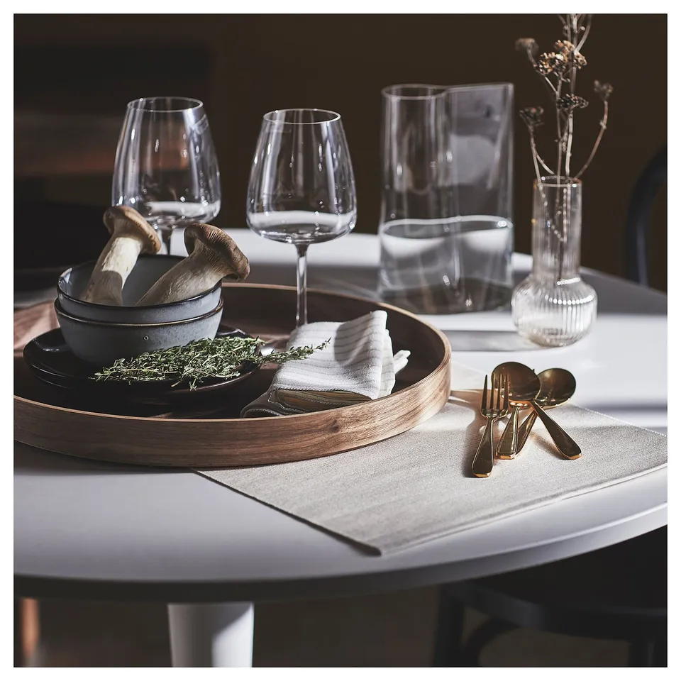 Grey place mat, wooden tray, herbs, mushrooms, cloth, gold cutlery, wine glasses, vase with dried flowers.