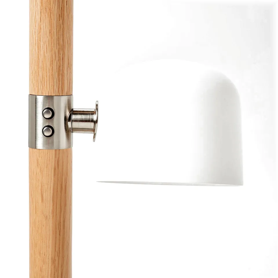 Close-up of modern lamp joint: polished metal connector attaches sleek white shade to smooth wooden pole.