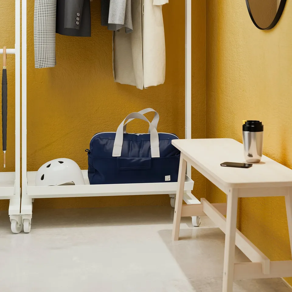 Office vegan leather bag, helmet, and metal cup on rolling clothes rail and table.