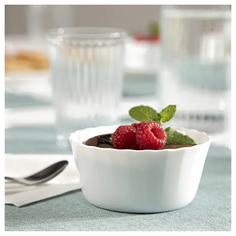 Ceramic bowl with chocolate mousse, raspberries, and mint on blue cloth, glass beside.