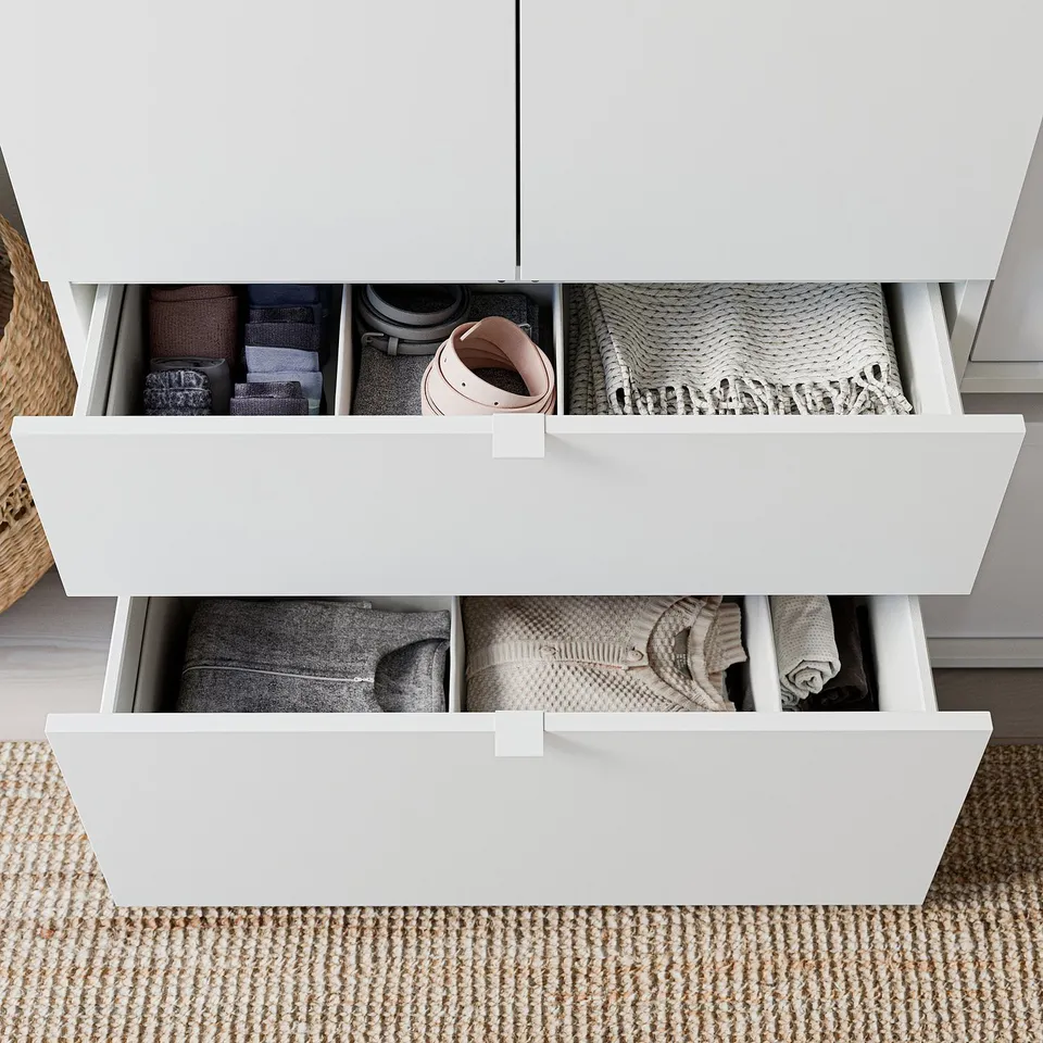 Organised white drawers with mixed textiles. Top drawer holds folded clothes, belt, scarf. Bottom drawer stores more folded garments.