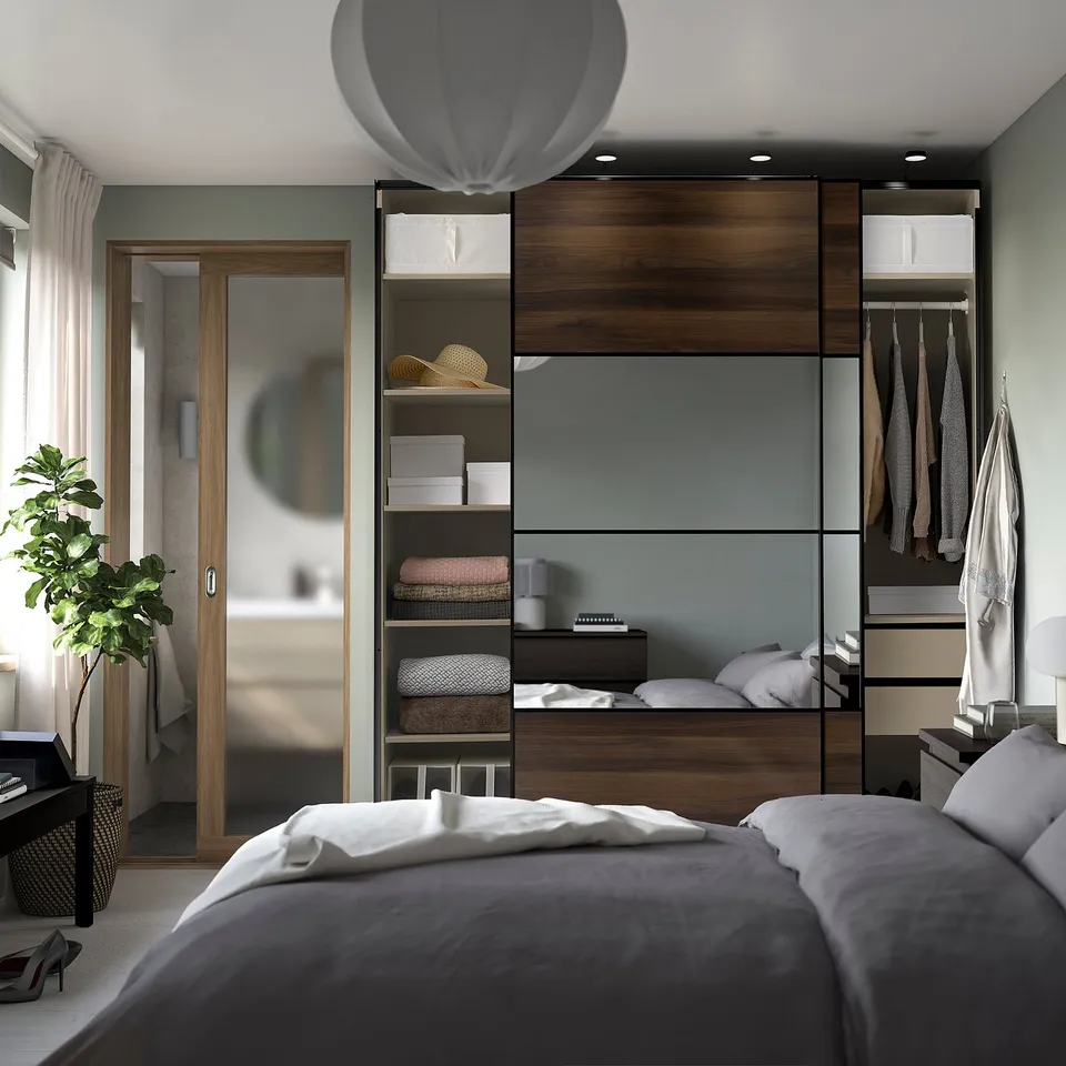 Modern bedroom with PAX wardrobe featuring mirrored sliding doors, shelves, and hanging space. Complete with a bed and plants.