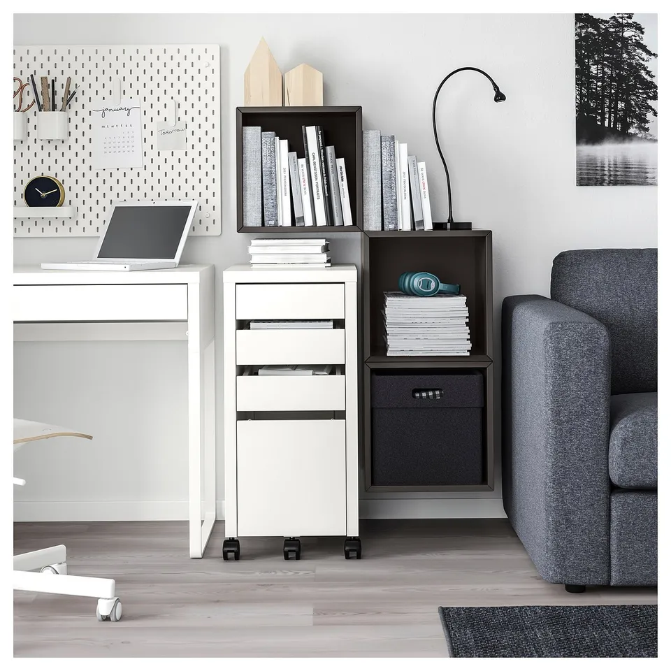 Modern home office with white EKET storage units, grey fabric couch, laptop on white desk, and black and white decor.