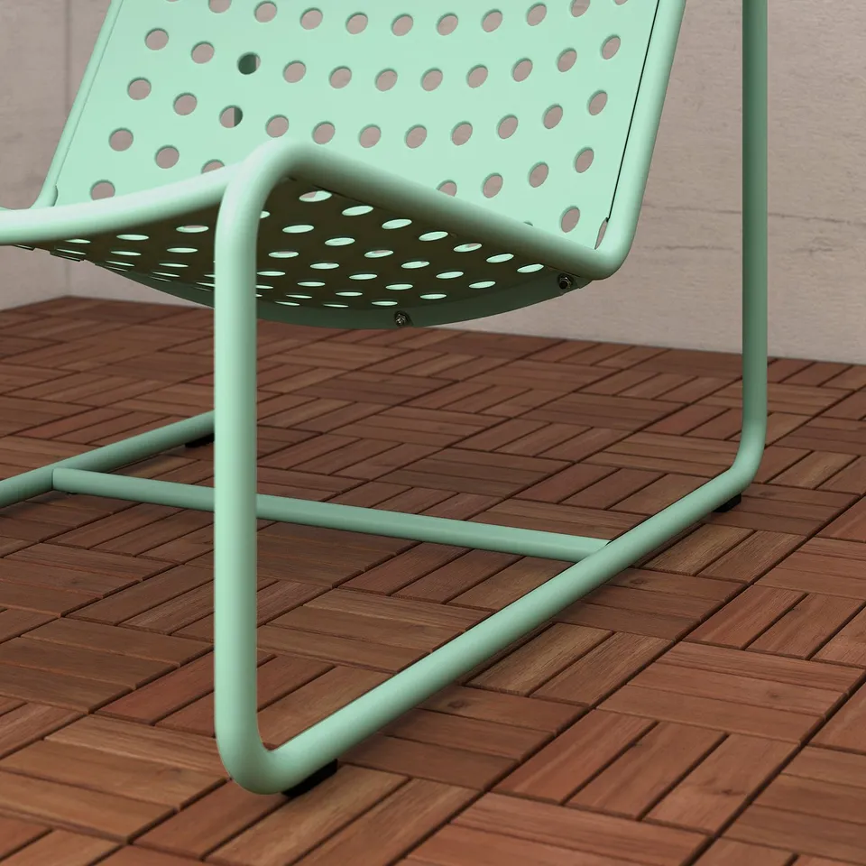 Modern mint-green metal chair on wooden deck. Perforated seat, sturdy design.