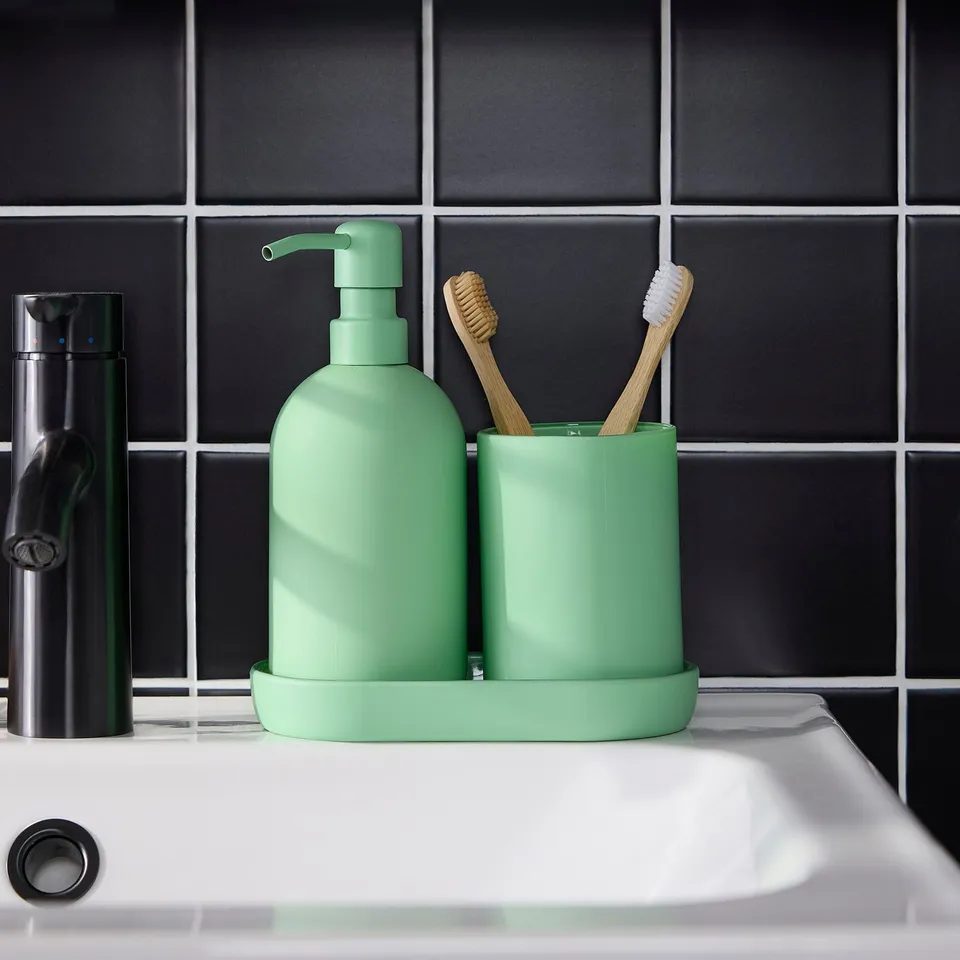 Green glass soap dispenser and toothbrush holder with tray on sink, modern bathroom decor.