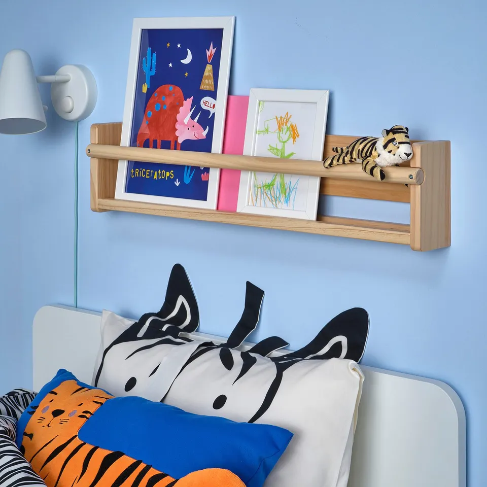 Kids bedroom with blue wall, wooden shelf, bed with pillows, wall light.