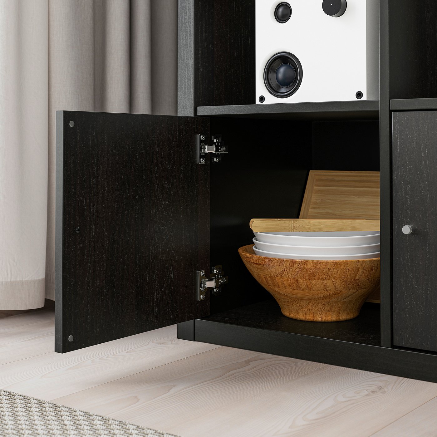 Black KALLAX shelf unit with open door revealing wooden bowl, plates, and cutting board, demonstrating storage versatility.
