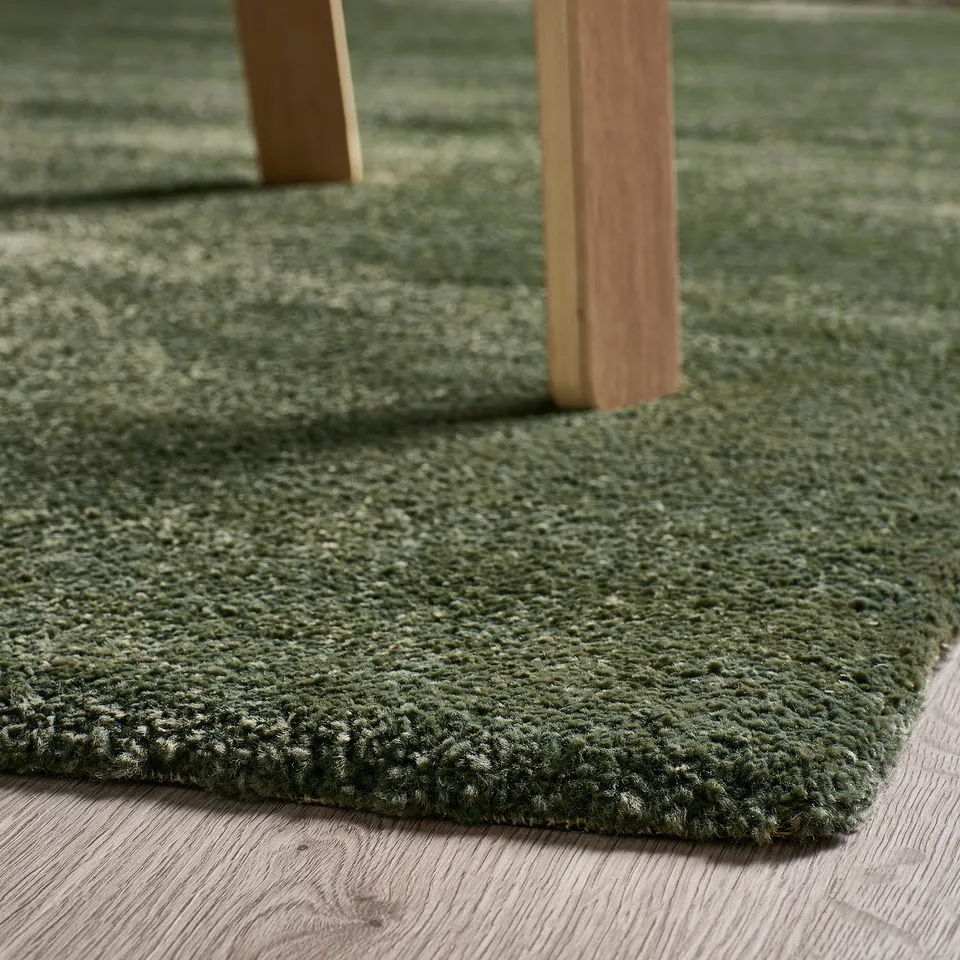 Green textured area rug on wooden floor, with table legs on it.