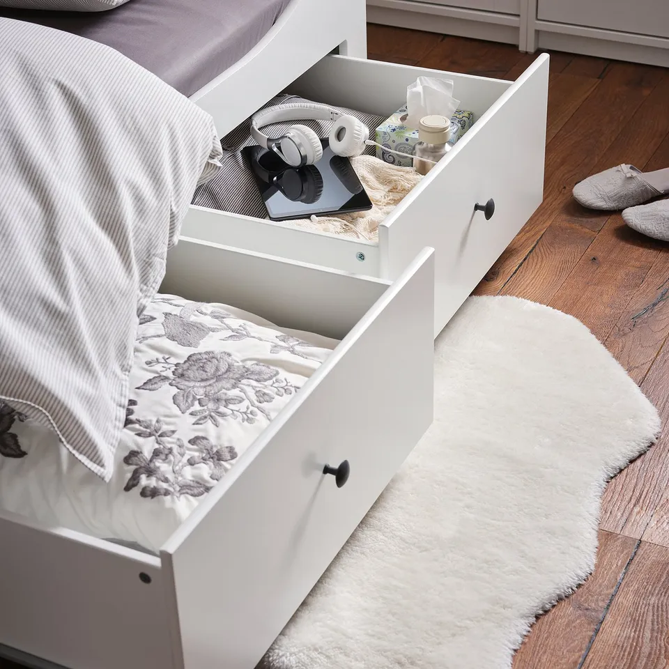 Bed with open drawers storing items. One drawer has a floral blanket, the other holds personal care items.