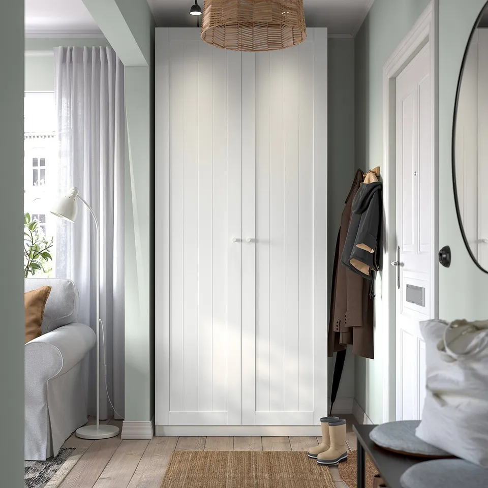 Entryway with large white PAX wardrobe, coat hooks, sofa, and lamp beside window.