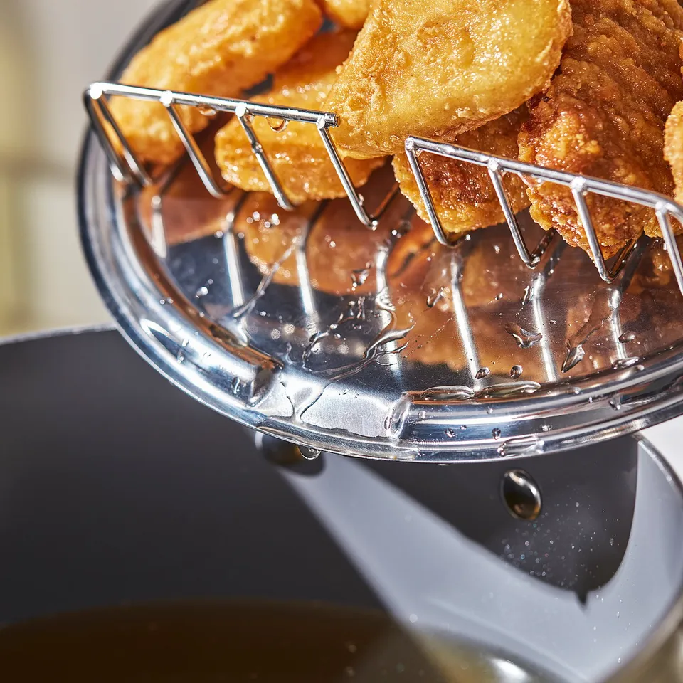 A close-up of a frying basket lifting golden fried foods from hot oil, showcasing the efficient draining and cooking function.