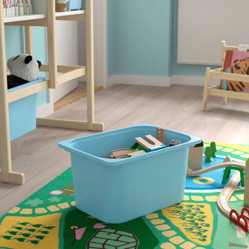 Light blue toy bin with wooden blocks, on a colourful play rug, next to wooden train tracks; part of a childrens storage and play setup.