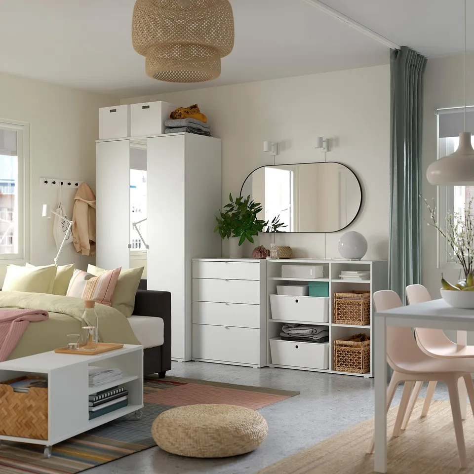 Modern living room with pink chairs, white furniture, green plants, and a large light fixture.