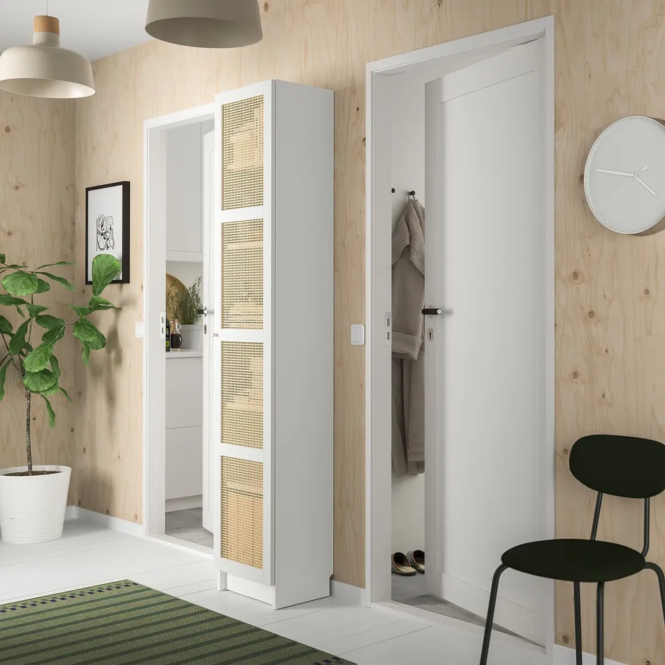 Modern entryway with white BILLY bookcase, wooden walls, black chair, green plant, and coat hooks.