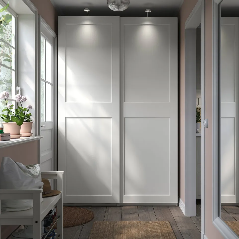 Modern, minimalist white wardrobe with sliding doors featuring built-in lighting and plant decor.