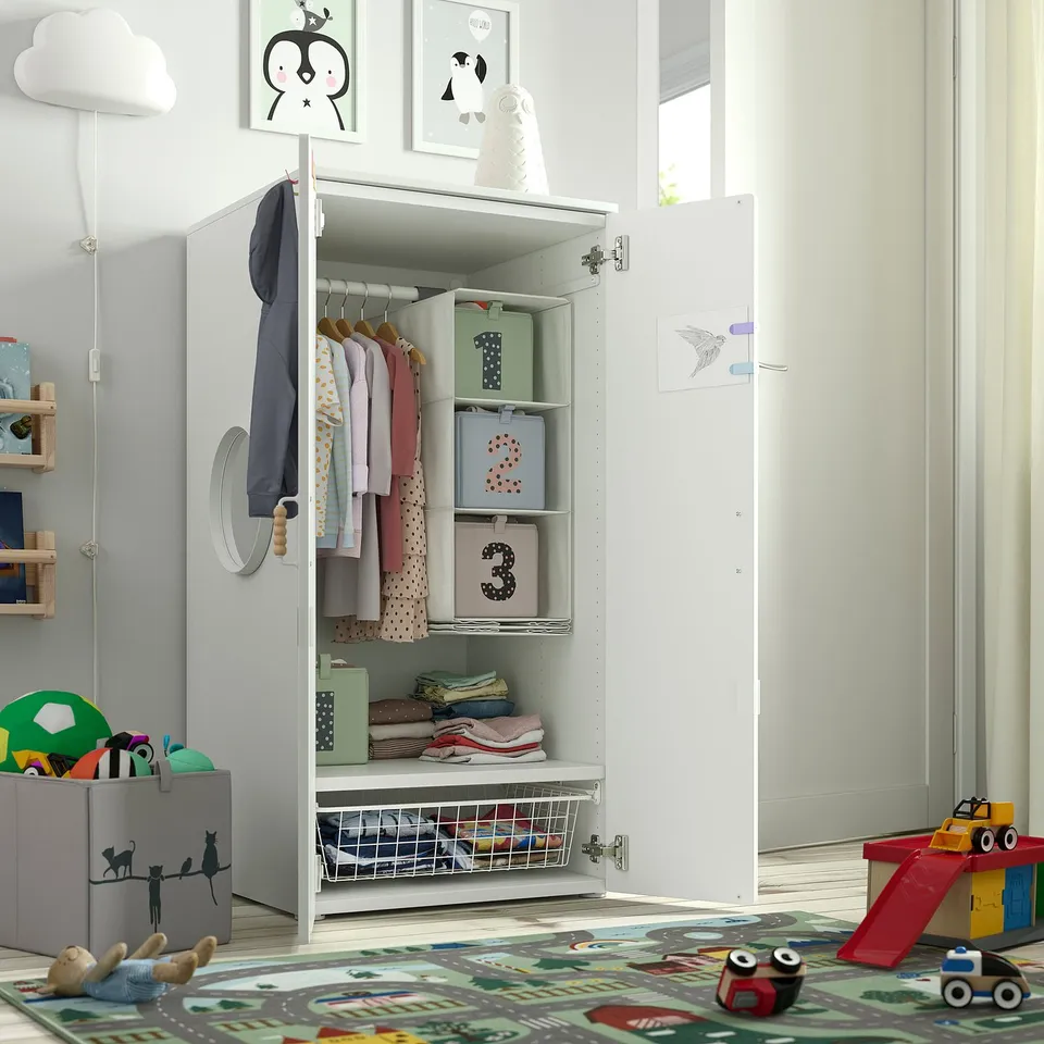 Childs room with SMÅSTAD wardrobe. Wardrobe open, showing clothes, boxes, and shelf. Soft close doors. Adjustable, child-friendly height.