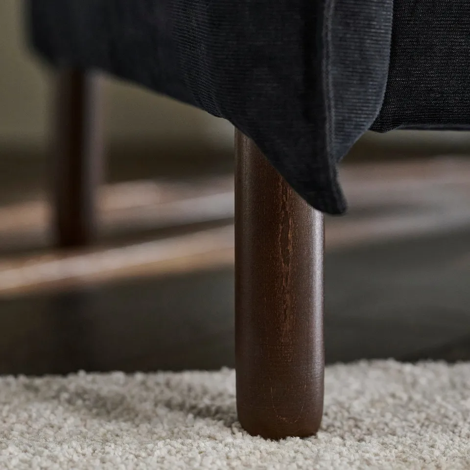 A close-up of a sofa leg, smooth and sturdy wood, dark finish, soft cushions visible.