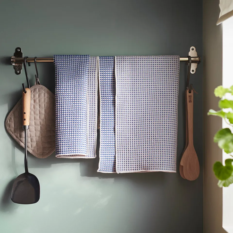 Blue and white waffle-textured towels hang on wall hooks near kitchen utensils and plants.