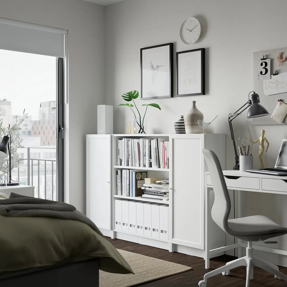 A modern bedroom with BILLY bookcase, desk, chair, grey walls, art, clock, and natural light.