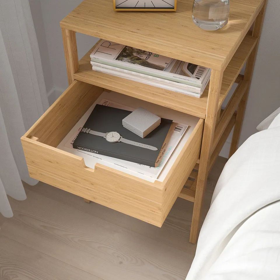 Wooden bedside table with open drawer showing books and box; stylish clock and glass on top.