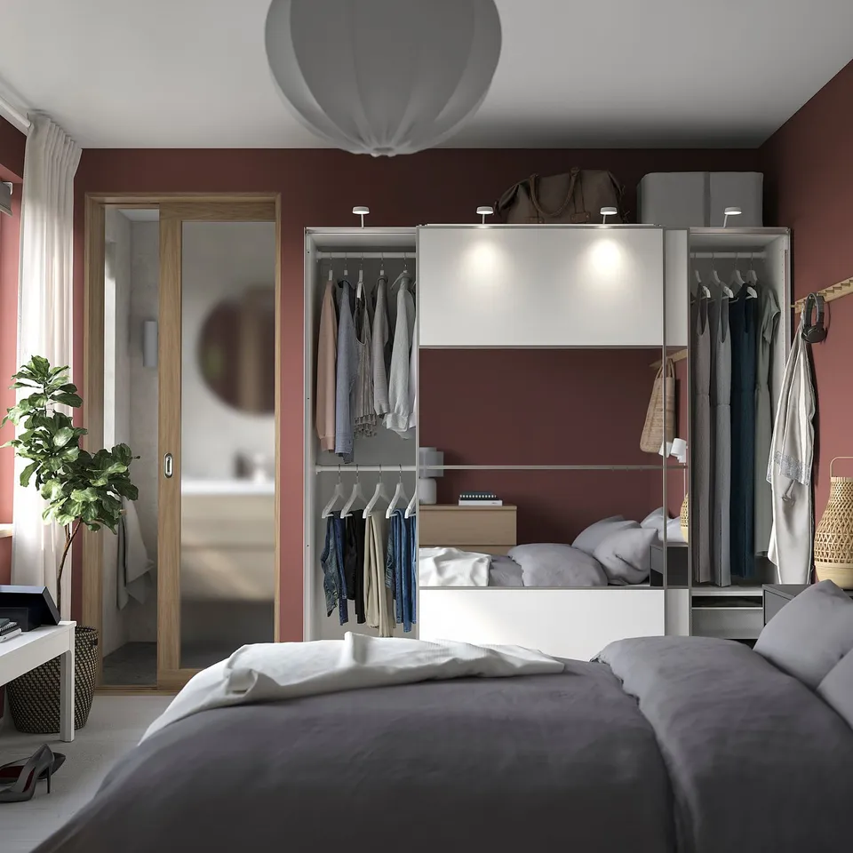Modern bedroom with maroon walls, white linens, PAX wardrobe, mirror, pendant light.