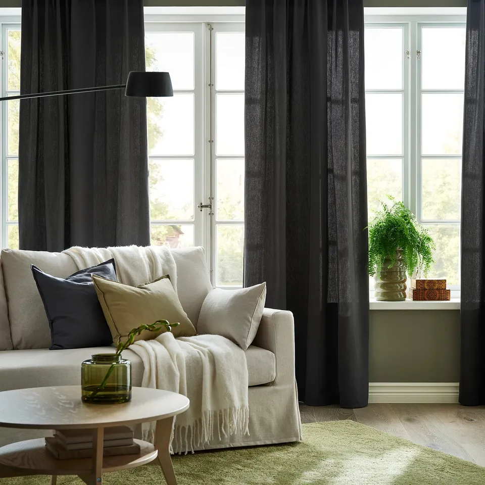 Living room with dark grey curtains, white armchair, coffee table, green vase.