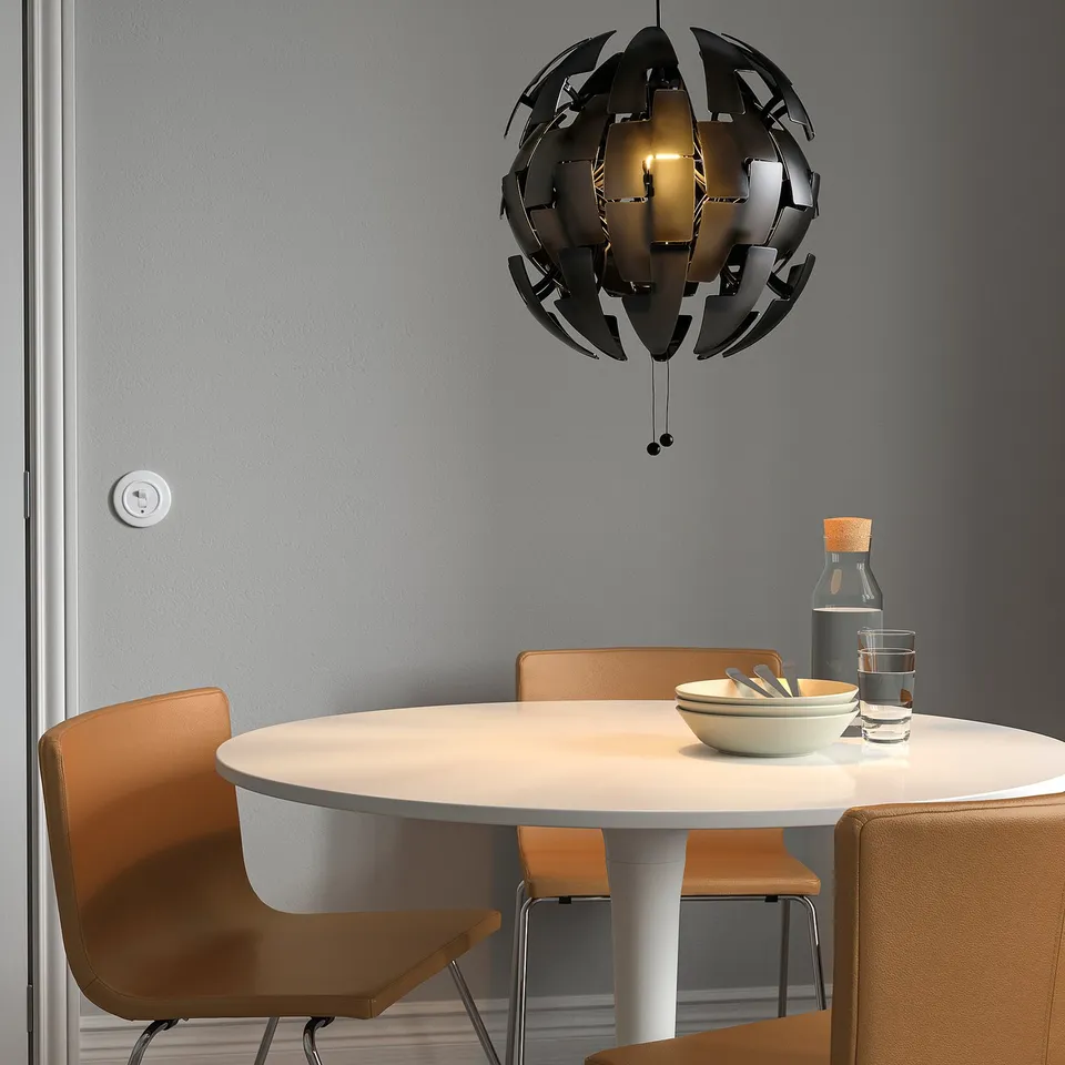 Modern dining setup with IKEA PS 2014 black pendant lamp, orange chairs, and table with bowl, glasses, and bottle.