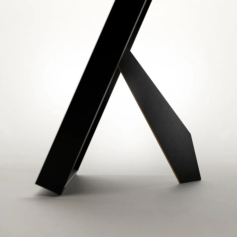Black picture frame standing on a table, angled to show front and side profile, demonstrating its versatile display options.