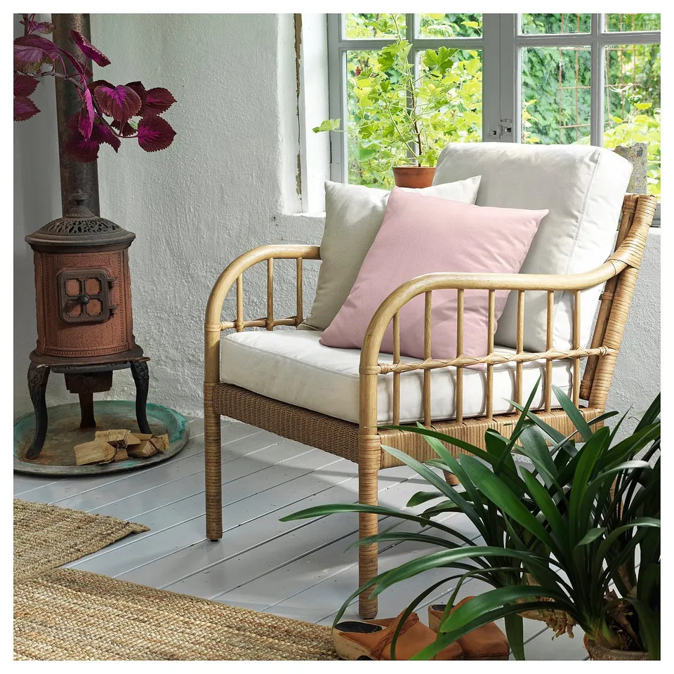 The HOLMSTA wicker chair with light cushions, wood stove, and plants.