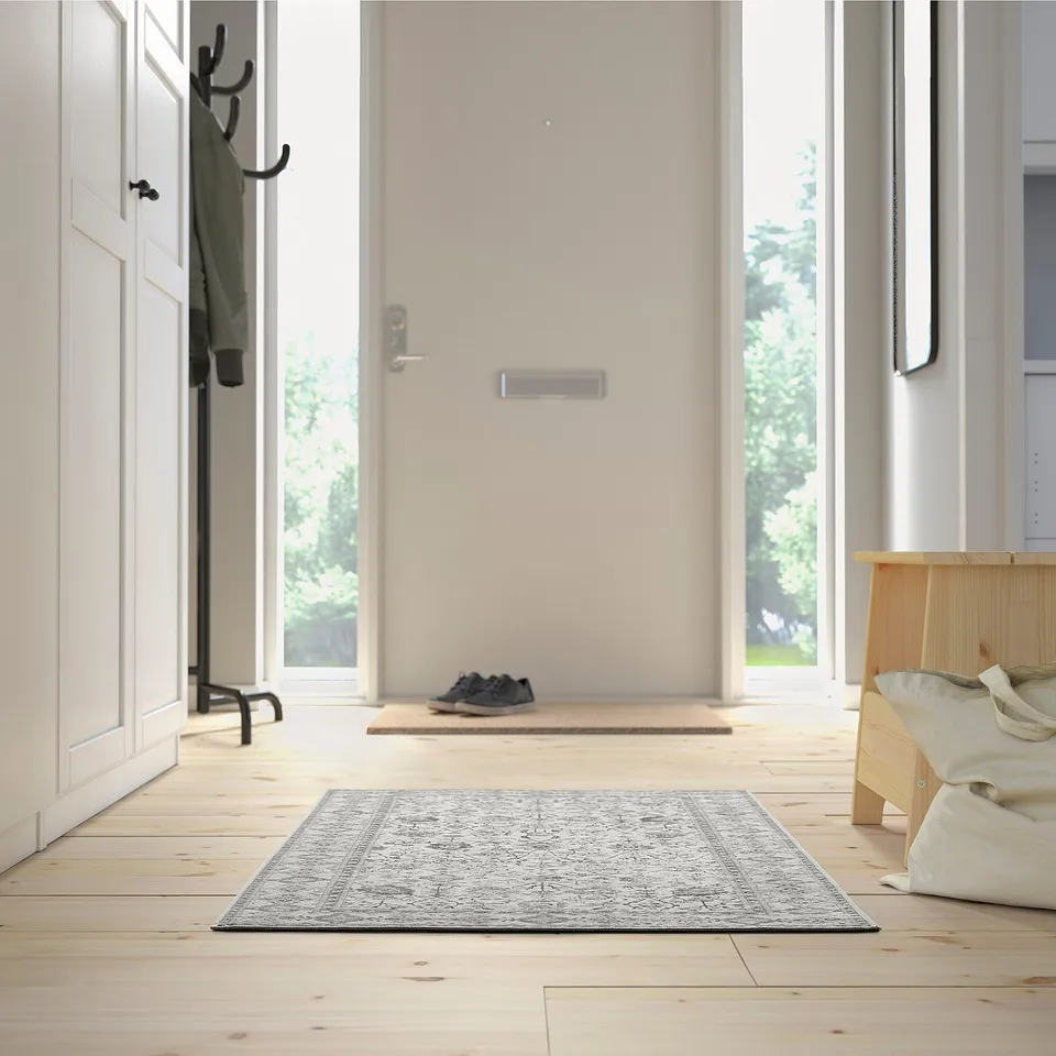 Wooden entryway with rug, bench, and shoes on mat.