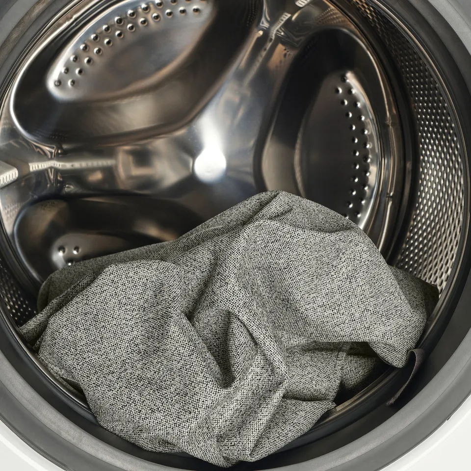 Image shows a washing machine with a grey fabric item inside, likely a removable cover for a bed frame, designed for easy cleaning.
