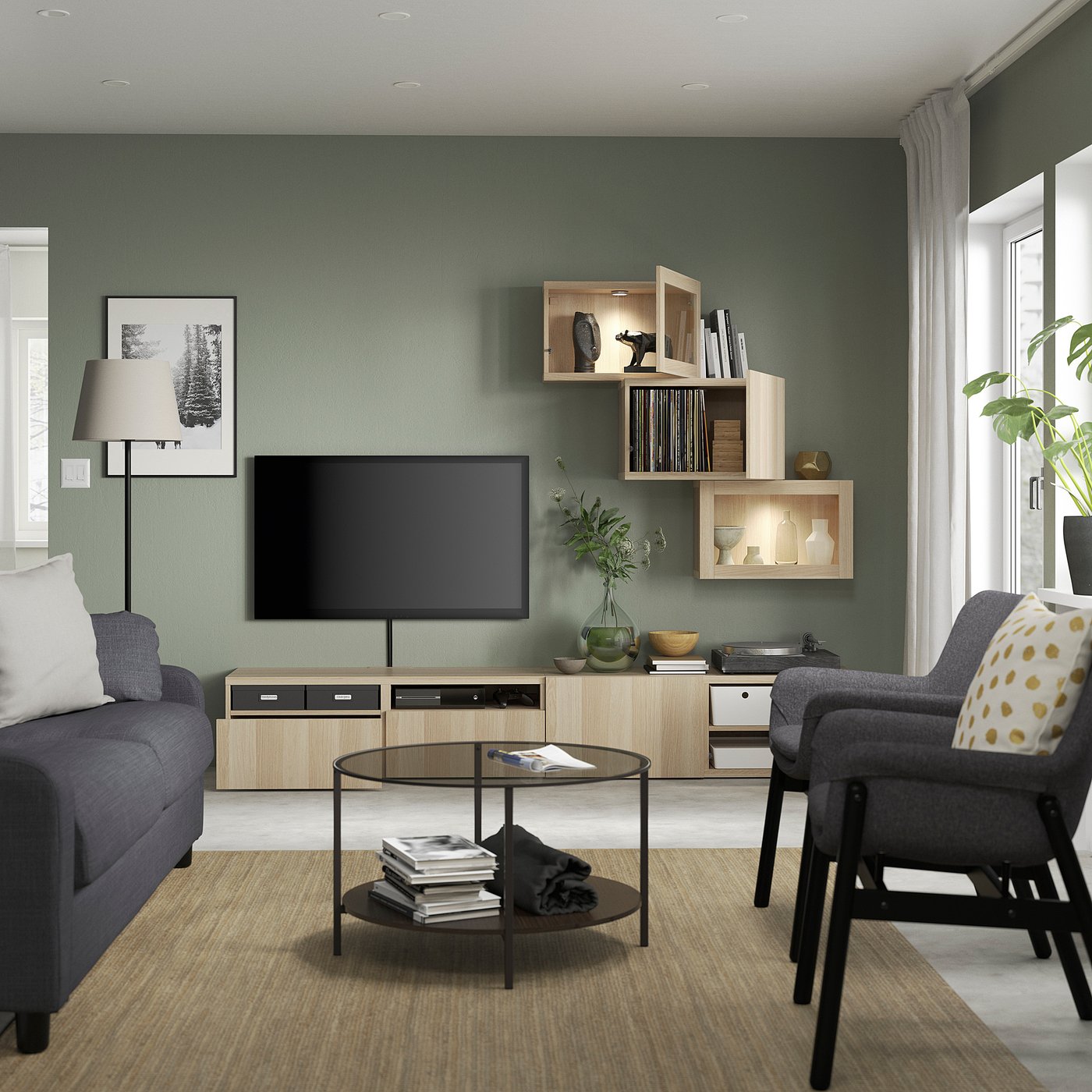 Modern living room with green walls, grey couch, circular glass coffee table, flat screen tv, and wooden shelves.