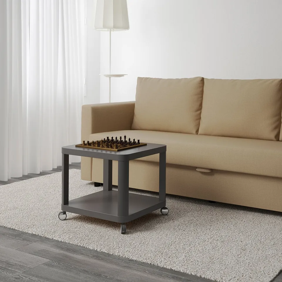 Modern living room with beige sofa, small black coffee table on wheels with chess set, and large window with white curtains.