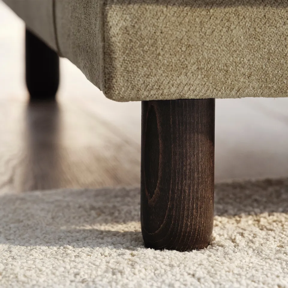 Close-up of sofa leg on plush carpet. Sturdy, dark wood with smooth finish, showing robust craftsmanship.