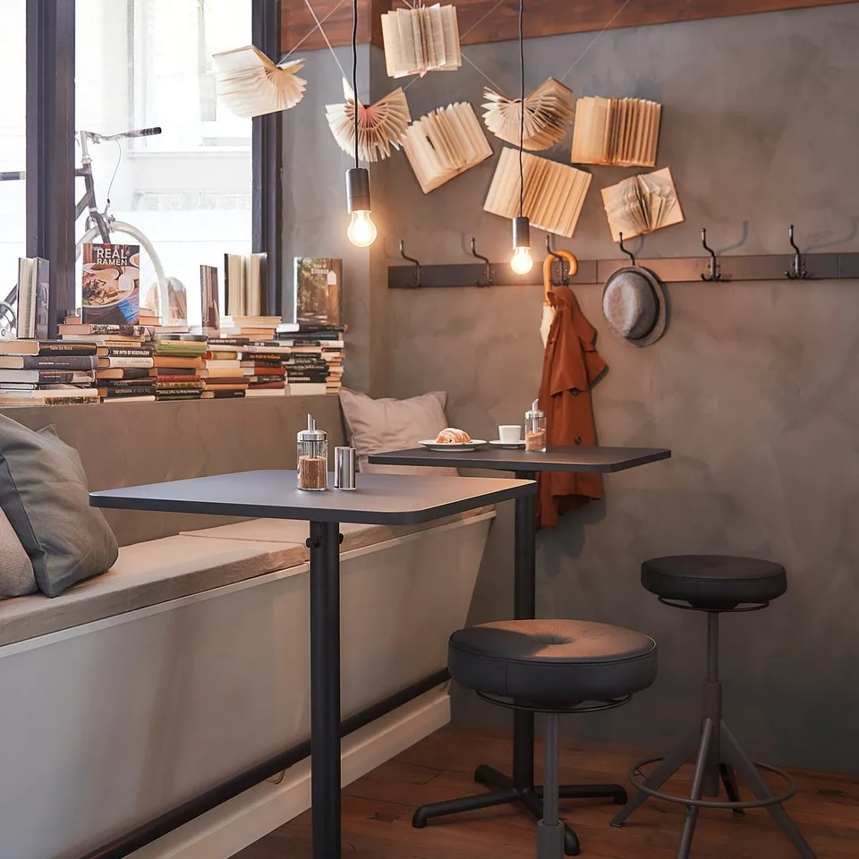 Modern café seating area with square black bar tables and stools, wooden floors, and unique light fixtures.