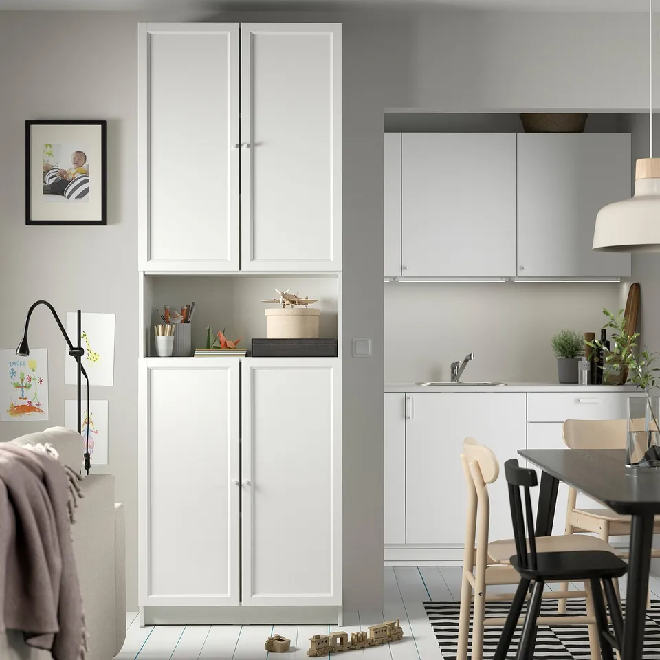 Modern, white BILLY bookcase in living area, featuring open shelving with decorative items and closed storage, flanked by wall-mounted baby artwork.