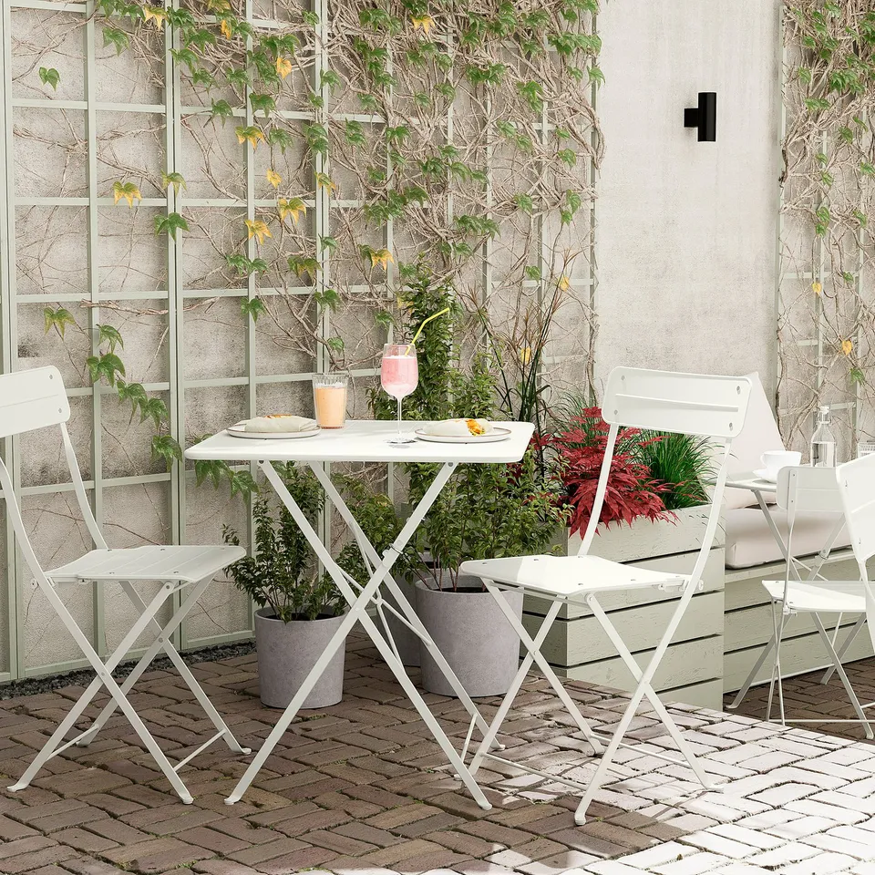 Small outdoor setup with white foldable table and chairs, potted plants, glasses, plates. Perfect for balconies.