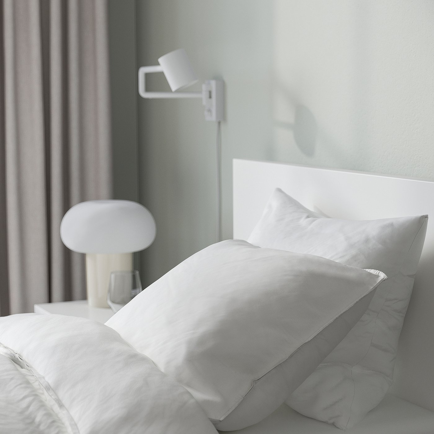 Modern bed with high headboard, grey curtains, and white lamp on side table, offering soft lighting.