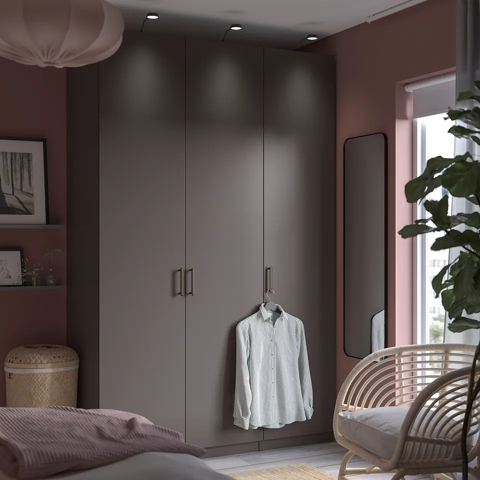 Modern bedroom featuring a grey PAX wardrobe with a hanging shirt, next to a wicker chair and a potted plant by the window.