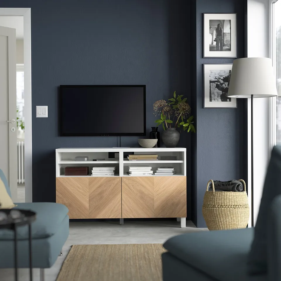 Modern living room: dark blue walls, BESTÅ tv bench, tv, blue sofa, lamp, pictures, storage.