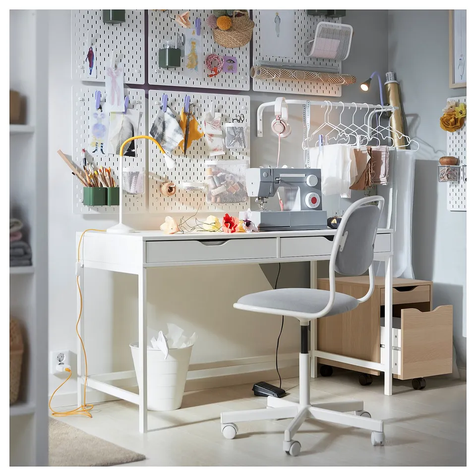 Organised workspace with white ALEX desk and grey chair, pegboard with accessories, sewing machine, and storage units.